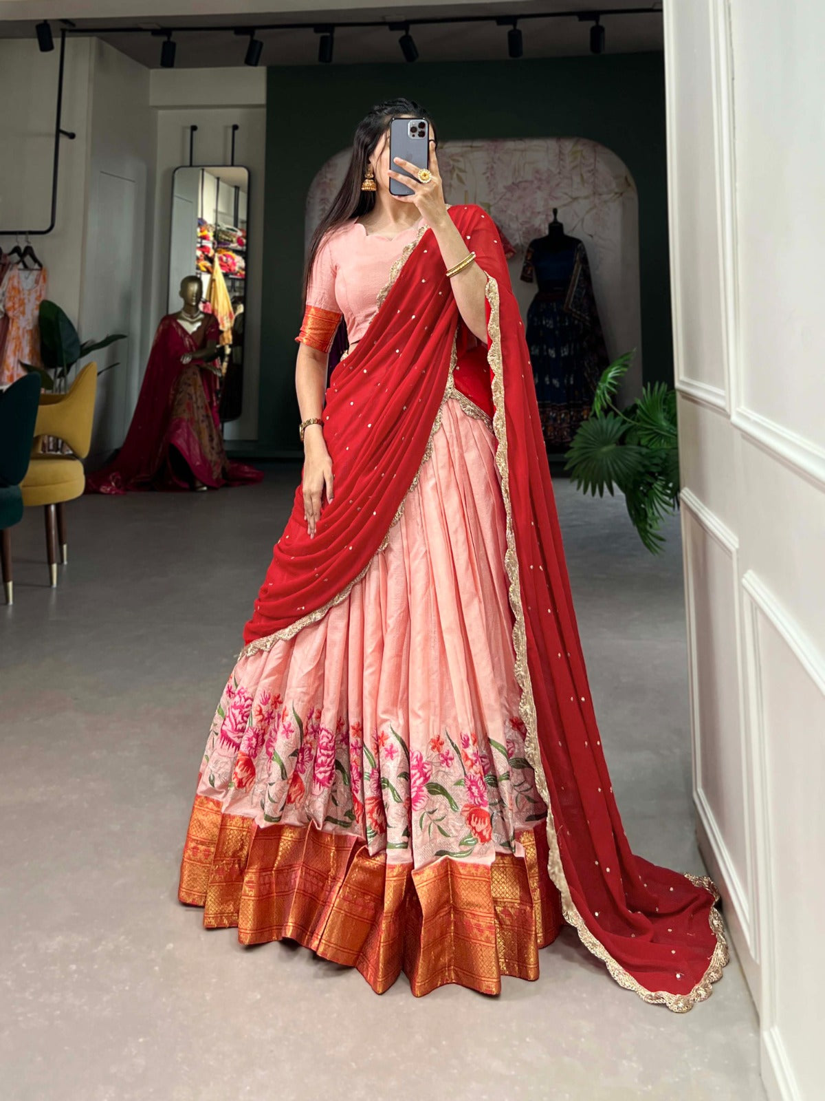 Woman wearing a traditional saree with a red blouse and pink skirt in a room.