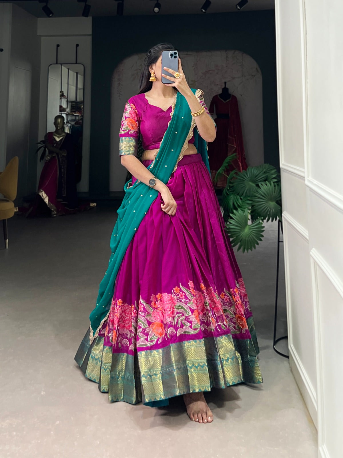 Woman taking a mirror selfie wearing a vibrant traditional outfit with a pink blouse and green saree.